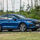 Błękitny Audi Q5 Sportback 2025 pędzi po drodze, otoczony zielenią i drzewami.