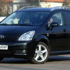 Czarny Toyota Corolla Verso z relingami dachowymi, zaparkowany na ulicy.