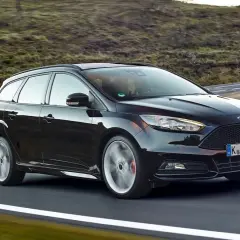 Czarny Ford Focus 3 kombi na zakręcie malowniczej drogi.