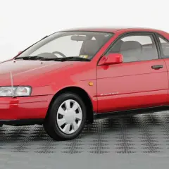 Czerwone, dwudrzwiowe Toyota Paseo z lat 90. na szarym, kratkowanym tle.