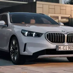 Białe BMW 550e z nowoczesnym grillem i światłami LED stoi przed minimalistycznym budynkiem.