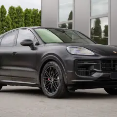 Matowy czarny Porsche Cayenne 2025 z czarnymi felgami stoi przed nowoczesnym budynkiem.