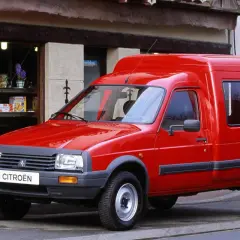 Czerwony van Citroen C15 zaparkowany przed sklepem z witryną pełną drobnych przedmiotów.