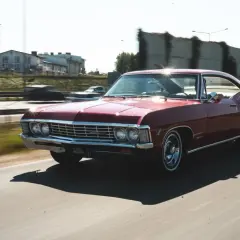 Czerwony Chevrolet Impala 1967 sunie po drodze, błyszcząc w słońcu. Klasyk w ruchu.