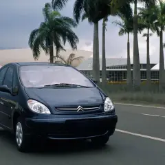 Ciemnoniebieski Citroen Xsara Picasso jedzie drogą wśród palm, w tle nowoczesna architektura.