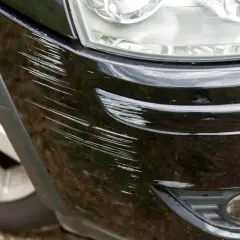 Zarysowany czarny zderzak Hyundai Kona Electric, obok reflektora i koła.