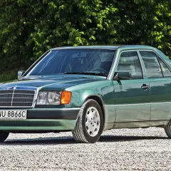 Zielony Mercedes 200 z lat 90. stoi na szutrowej drodze, otoczony zielenią.
