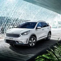Biały Kia Niro Hybrid stoi na drewnianej platformie, otoczony kaskadą wody.