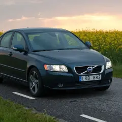 Ciemnozielone Volvo S40 2.0 diesel jedzie wiejską drogą pośród kwitnącego rzepaku.