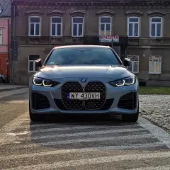 Szare BMW 420i z charakterystycznym grillem stoi na przejściu dla pieszych. W tle kamienice.