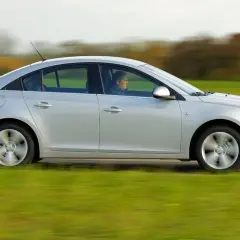 Srebrny Chevrolet Cruze 1.8 benzyna w ruchu, z kierowcą za kierownicą, przemierza wiejską drogę pośród zielonych pól.