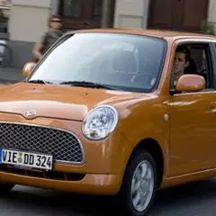Pomarańczowy Daihatsu Trevis z kierowcą za kierownicą jedzie ulicą.