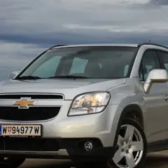 Srebrny Chevrolet Orlando na tle pochmurnego nieba i pól. Idealny na rodzinne wypady.
