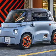 Niebieski Citroen Ami z pomarańczowymi felgami jedzie ulicą.