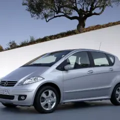 Srebrny Mercedes W169 stoi na tle białej ściany i drzewa oliwnego.