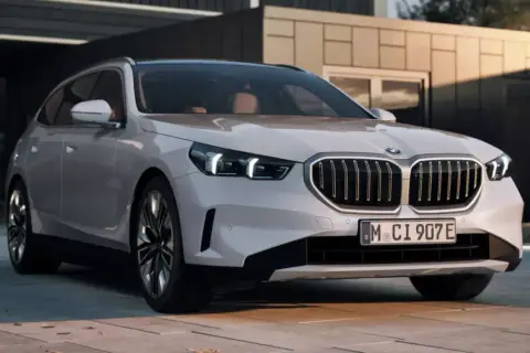 Białe BMW 550e z nowoczesnym grillem i światłami LED stoi przed minimalistycznym budynkiem.