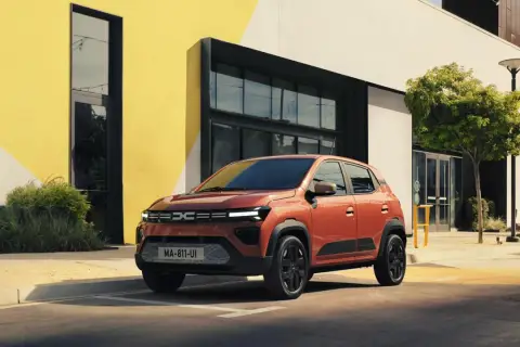 Pomarańczowy Dacia Spring stoi przed nowoczesnym budynkiem. Sprawdź atrakcyjną dacia spring cena!