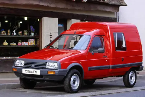 Czerwony van Citroen C15 zaparkowany przed sklepem z witryną pełną drobnych przedmiotów.