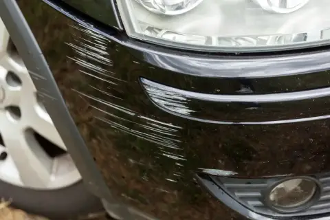 Zarysowany czarny zderzak Hyundai Kona Electric, obok reflektora i koła.