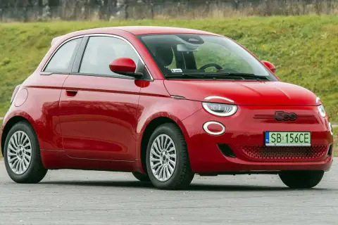 Czerwony fiat elektryczny 500 na tle zielonej skarpy.