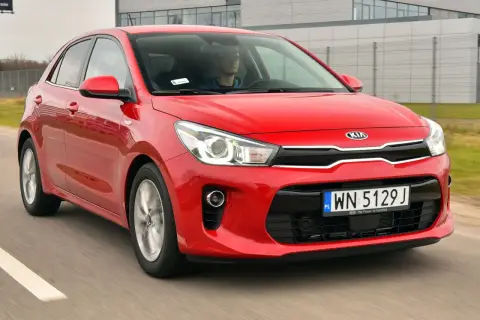 Czerwony **Kia Rio 4** w ruchu drogowym, z kierowcą za kierownicą.