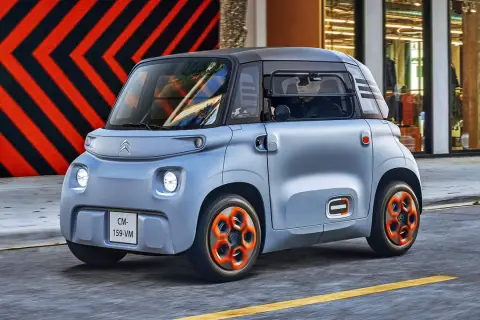 Niebieski Citroen Ami z pomarańczowymi felgami jedzie ulicą.