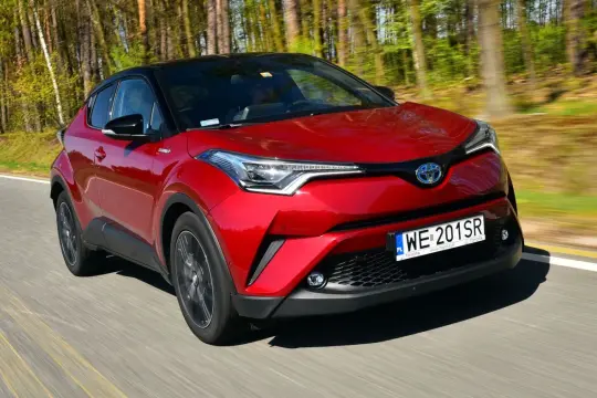 Czerwona Toyota C-HR Hybrid pędzi leśną drogą.
