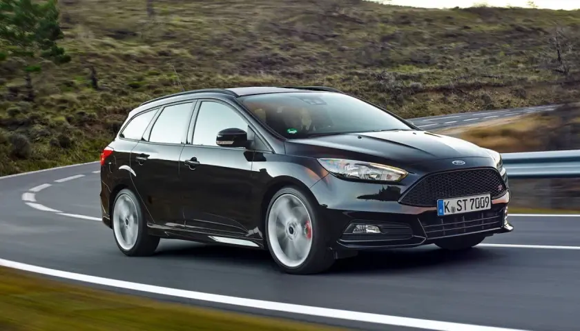 Czarny Ford Focus 3 kombi na zakręcie malowniczej drogi.