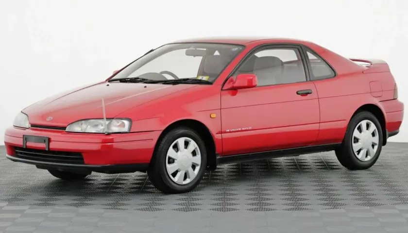 Czerwone, dwudrzwiowe Toyota Paseo z lat 90. na szarym, kratkowanym tle.