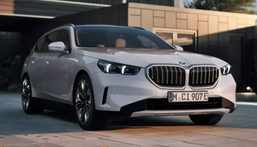 Białe BMW 550e z nowoczesnym grillem i światłami LED stoi przed minimalistycznym budynkiem.