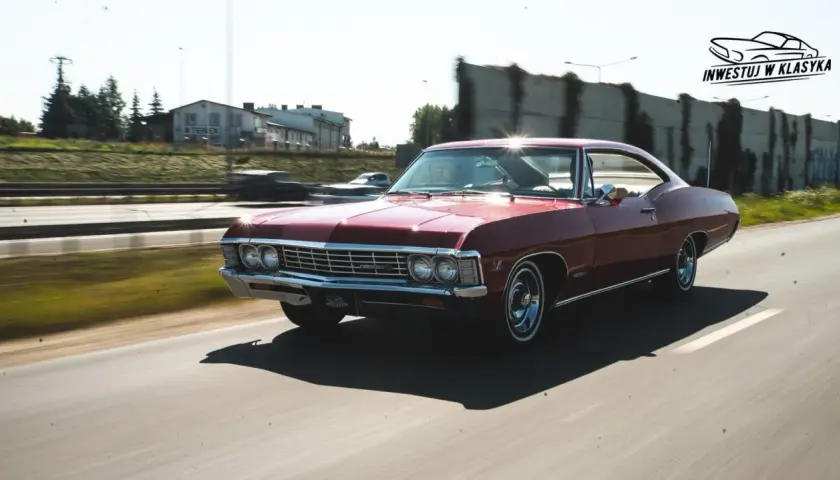 Czerwony Chevrolet Impala 1967 sunie po drodze, błyszcząc w słońcu. Klasyk w ruchu.