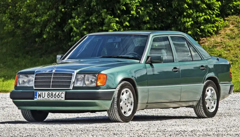 Zielony Mercedes 200 z lat 90. stoi na szutrowej drodze, otoczony zielenią.