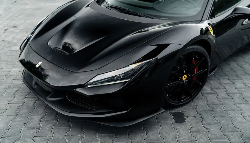 Czarny Ferrari F8 z błyszczącym lakierem i czerwonymi zaciskami hamulcowymi na czarnych felgach, zaparkowany na kostce brukowej.