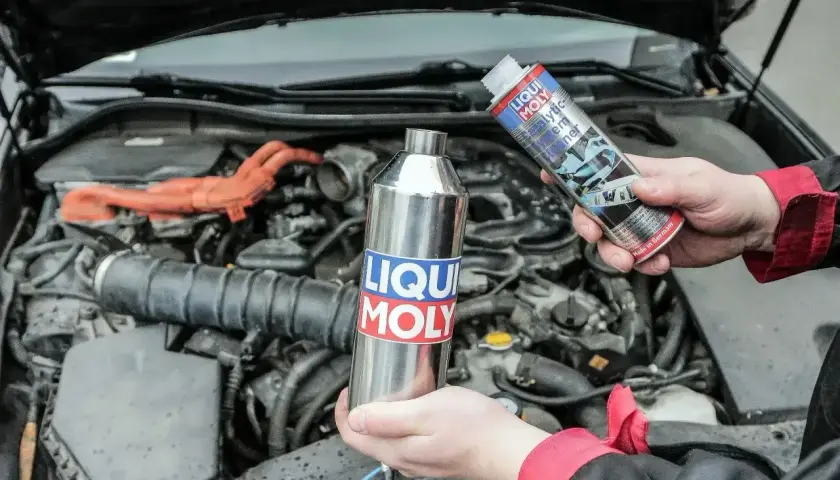 Czyszczenie katalizatora za pomocą preparatu Liqui Moly. Dwie ręce trzymają metalową butelkę i puszkę z płynem.