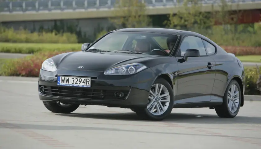 Czarny Hyundai Coupe 2.7 V6 z przyciemnionymi szybami i sportowymi felgami, zaparkowany na zewnątrz.