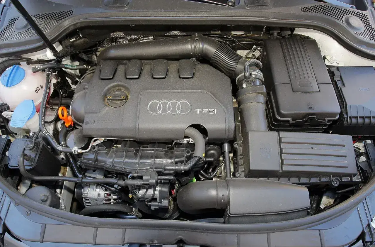 Silnik TFSI w Audi 8P, widok z góry. Widać pokrywę silnika z logo Audi, elementy układu dolotowego i filtry.