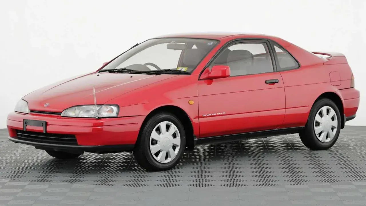 Czerwone, dwudrzwiowe Toyota Paseo z lat 90. na szarym, kratkowanym tle.