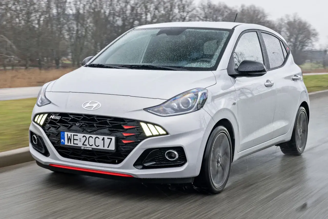 Biały Hyundai i10 N Line w ruchu, z widocznym grillem i światłami. Sprawdź aktualną hyundai i10 cena.