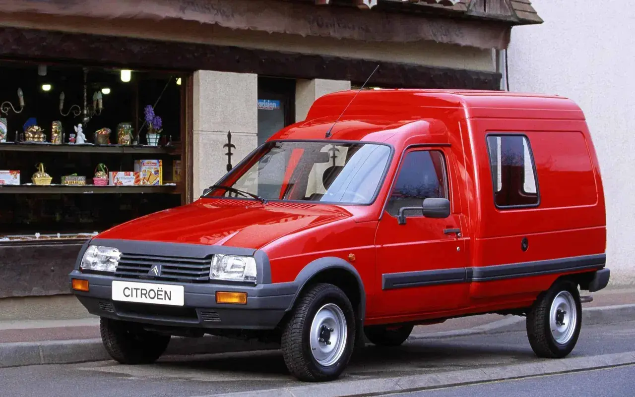 Czerwony van Citroen C15 zaparkowany przed sklepem z witryną pełną drobnych przedmiotów.