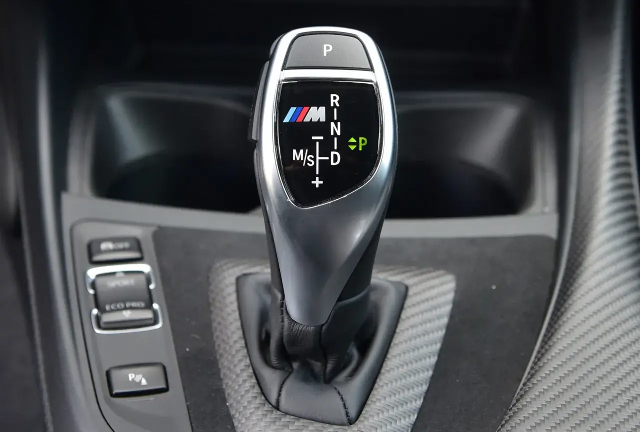Oznaczenia automatycznej skrzyni biegów BMW M: P, R, N, D, M/S. Widoczny przycisk P i wybór trybów Sport/Eco Pro.