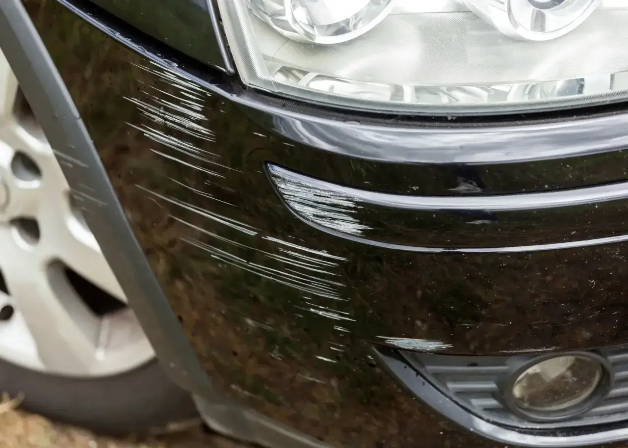 Zarysowany czarny zderzak Hyundai Kona Electric, obok reflektora i koła.