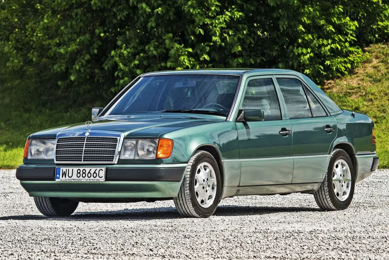 Zielony Mercedes 200 z lat 90. stoi na szutrowej drodze, otoczony zielenią.