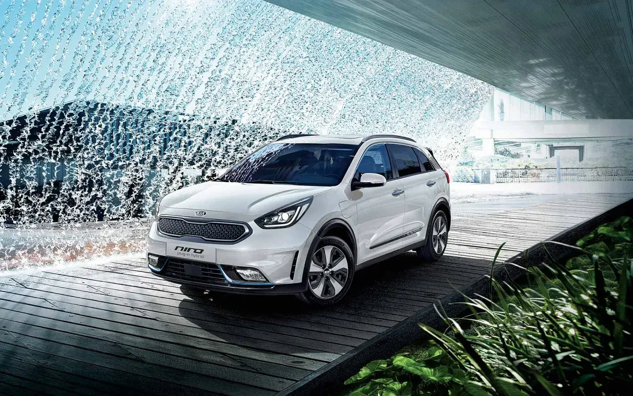 Biały Kia Niro Hybrid stoi na drewnianej platformie, otoczony kaskadą wody.