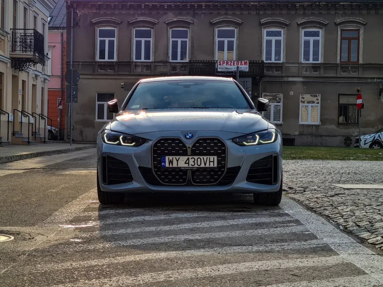 Szare BMW 420i z charakterystycznym grillem stoi na przejściu dla pieszych. W tle kamienice.