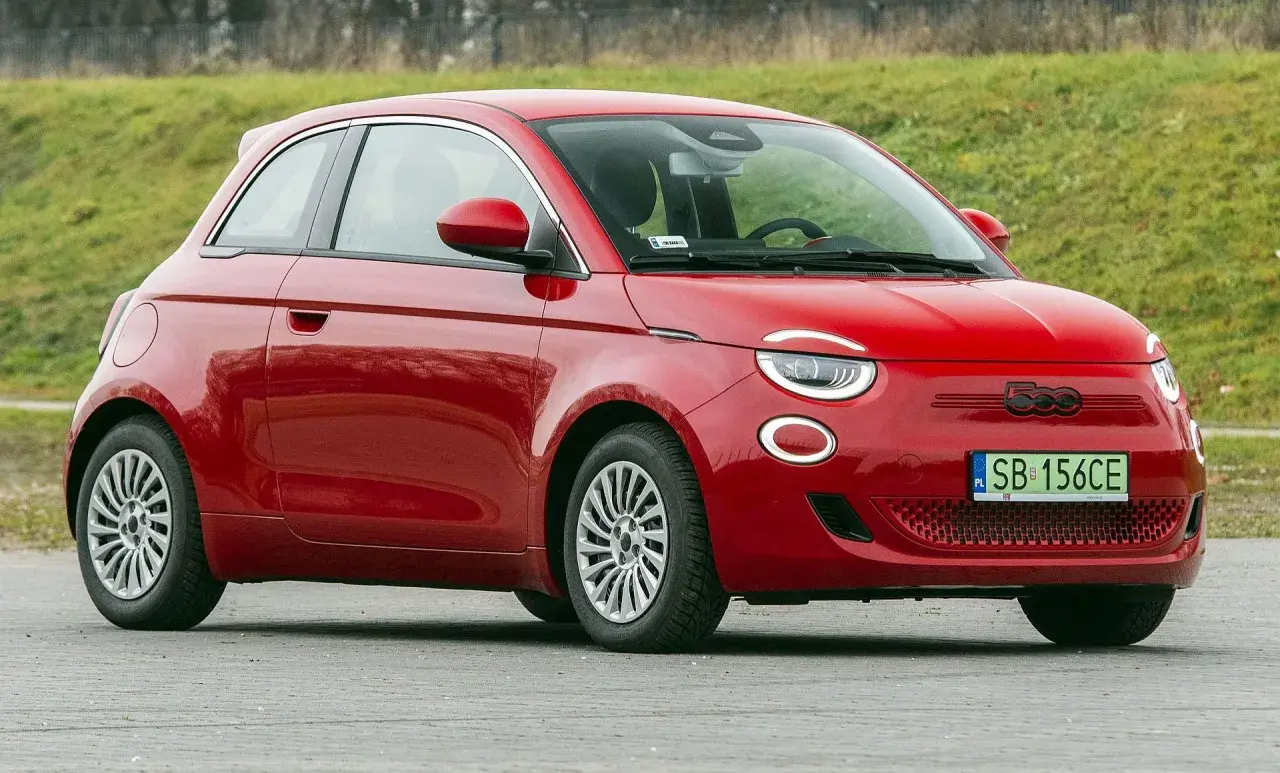 Czerwony fiat elektryczny 500 na tle zielonej skarpy.