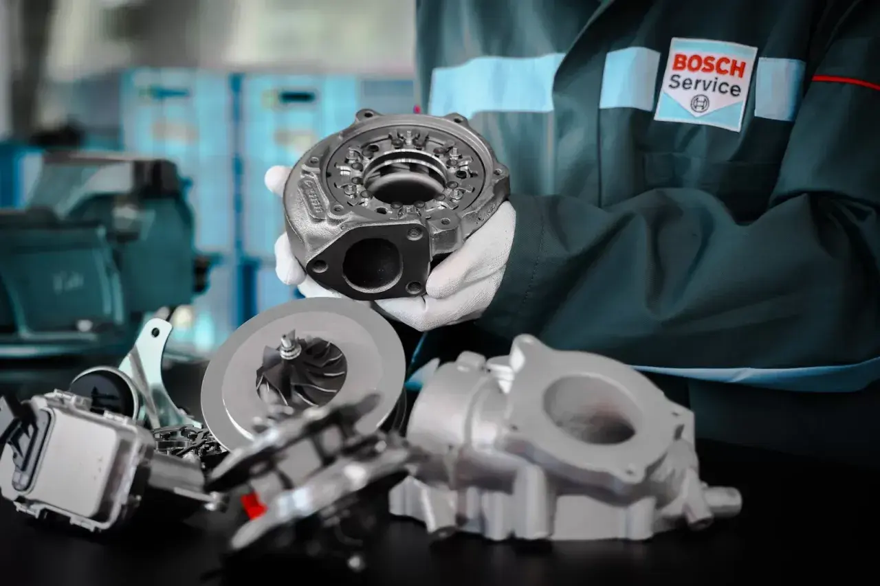 Mechanik w fartuchu Bosch Service prezentuje części turbosprężarki. Dowiedz się, ile kosztuje regeneracja turbiny i przywróć moc swojemu autu.