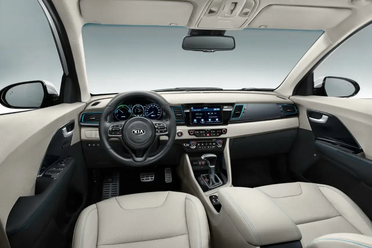 Wnętrze Kia Niro Hybrid: jasna tapicerka, kierownica z przyciskami, ekran multimedialny i dźwignia zmiany biegów.