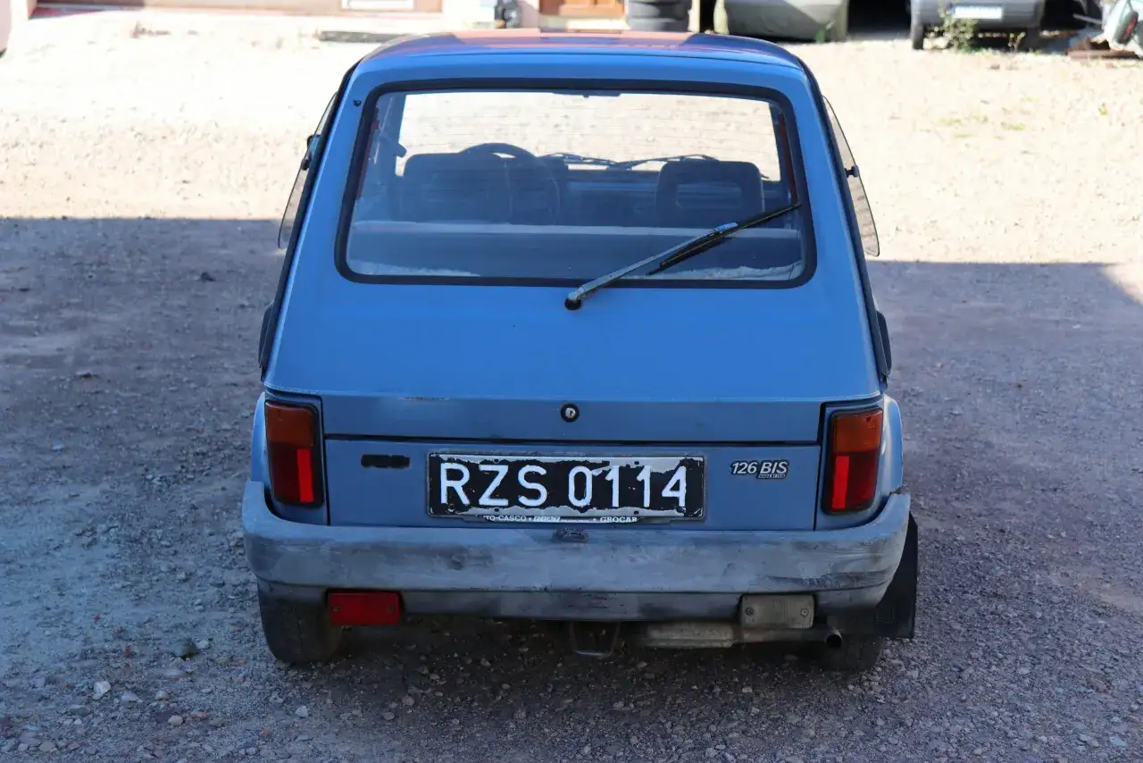 Niebieski Fiat 126p Bis z tablicą rejestracyjną RZS 0114 stoi na żwirowym podwórku.