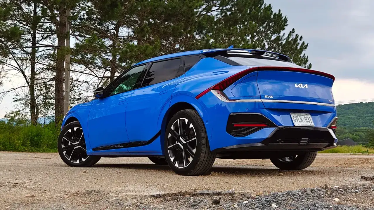 Niebieski Kia EV6 GT zaparkowany na żwirowej drodze, otoczony drzewami.
