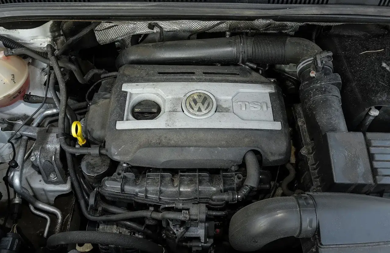 Silnik 2.0 TSI Volkswagena, widok z góry. Widać pokrywę silnika z logo VW i napisem TSI, przewody i inne elementy komory silnika.